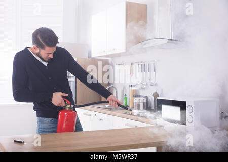 Junger Mann Spritzen Feuerlöscher auf Mikrowelle in der Küche Stockfoto