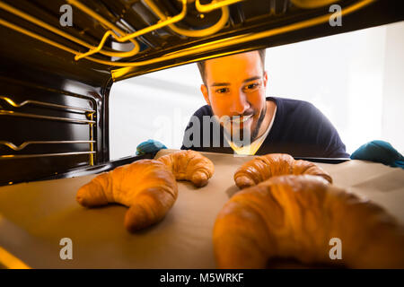 Glückliche junge Mann nehmen Sie Fach der gebackenen Croissants aus dem Ofen Stockfoto