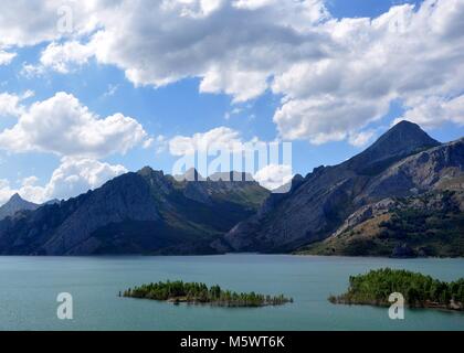 Blick über einen See in Nordspanien. Insel in See und Bergkette dahinter mit blauem Himmel und Wolken. Stockfoto