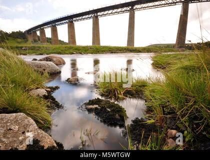 Eisenbahnbrücke über einen Fluss mit Reflexion, langer Belichtung und felsigen Vordergrund. Aufgenommen in Schottland Stockfoto