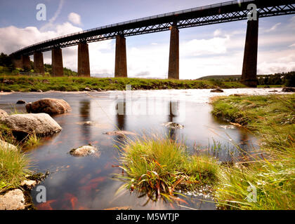 Eisenbahnbrücke über einen Fluss mit Reflexion, langer Belichtung und felsigen Vordergrund. Aufgenommen in Schottland Stockfoto