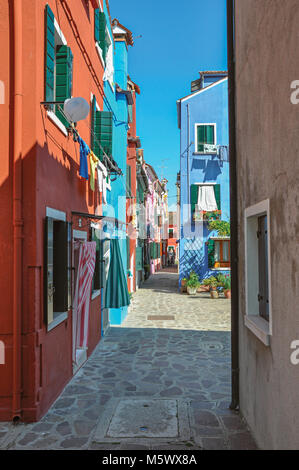 Überblick über die bunten Reihenhäuser und Kleidung hängend in einer Gasse an einem sonnigen Tag in Burano, eine liebenswürdige kleine Stadt voll von Kanälen, in der Nähe von Venedig. Stockfoto