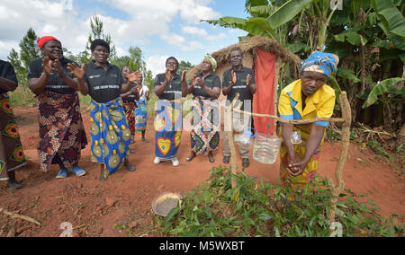 Die Mitglieder einer Community Care Gruppe singen über Hygiene als Frau verwendet eine Hand - Reinigung Station außerhalb einer Latrine in Kasangari Ngulube, Malawi. Stockfoto