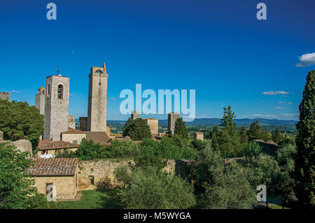 Aussicht auf die Dächer und Türme mit Bäumen und blauen sonnigen Himmel von San Gimignano. Eine mittelalterliche Stadt mit mehreren Türmen. Stockfoto