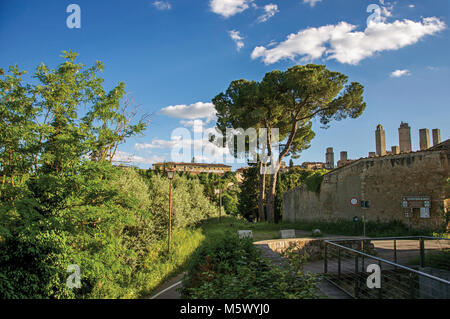 Blick auf die Stadtmauern und Türmen mit Bäumen am Sonnenuntergang in San Gimignano. Eine mittelalterliche Stadt mit mehreren Türmen. Stockfoto