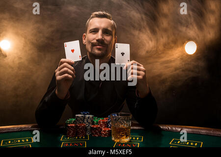 Der Mensch ist Poker spielen mit einer Zigarre und einem Whiskey, einem Mann zeigen zwei Karten in der Hand und gewann alle Chips auf dem Tisch mit dicken Zigarettenrauch. Stockfoto