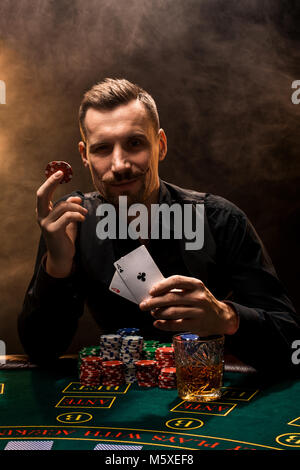 Der Mensch ist Poker spielen mit einer Zigarre und einem Whiskey, einem Mann zeigen zwei Karten in der Hand und gewann alle Chips auf dem Tisch mit dicken Zigarettenrauch. Stockfoto