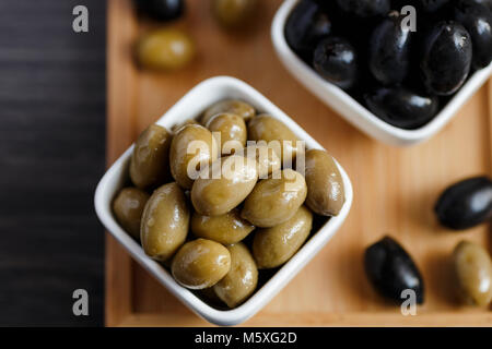 Schwarze und Grüne Oliven in einer weißen Schüssel auf einem dunklen Holztisch. Stockfoto