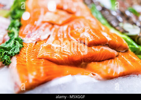 Fisch und Meeresfrüchte stehen mit Schnitten und Filets der orange gezüchtetem Lachs auf Eis mit Kale verlässt Stockfoto