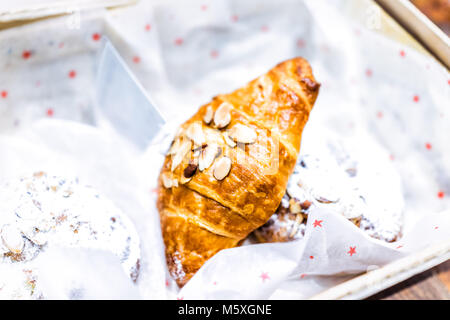 Nahaufnahme einer Mandel golden gebackenen frischen Croissant im Korb mit Gebäck Puderzucker desserts Süßigkeiten in Bäckerei cafe Store, home Einstellung Stockfoto