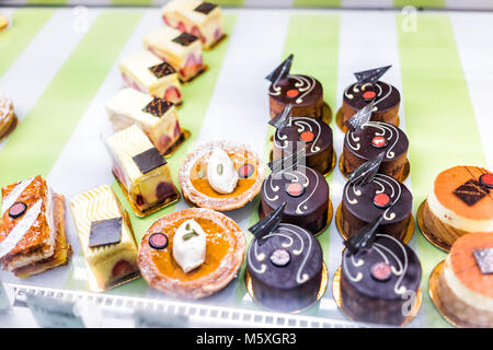 Viele verschiedene Auswahl Vielzahl von Mini kleine Schokolade Kuchen, Gebäck in der Bäckerei shop shop mit Halloween krebfarbigen Dekorationen hinter Glas Stockfoto