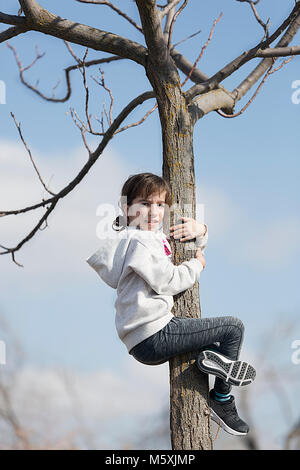 10-jährige Mädchen klettern auf einen Baum in die Kamera schaut. Horizontale shot mit Tageslicht Stockfoto