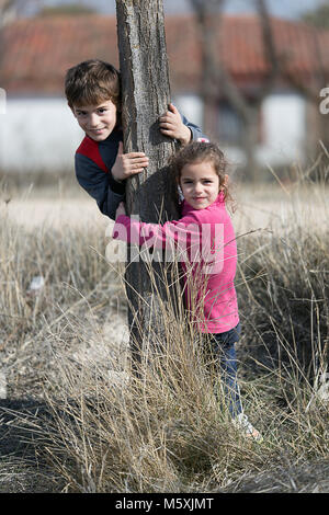 Zwei Kinder umarmen ein Stamm eines Baumes lächelnd. Horizontale shot mit Tageslicht Stockfoto