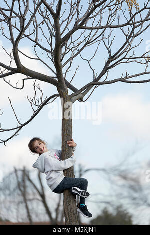 10-jährige Mädchen klettern auf einen Baum in Richtung Kamera schaut. Horizontale shot mit Tageslicht Stockfoto