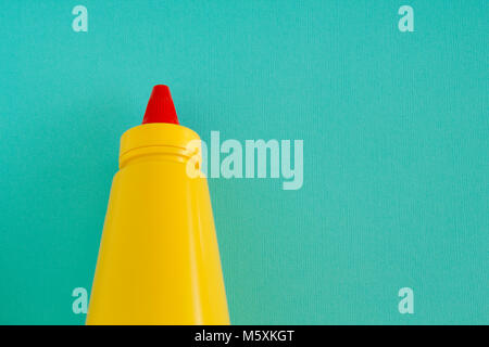 Eine helle gelbe squirting Senf oder Gewürz Flasche mit leuchtend roten verdrehen Deckel. Links auf ein aqua Hintergrund ausgerichtet. Stockfoto