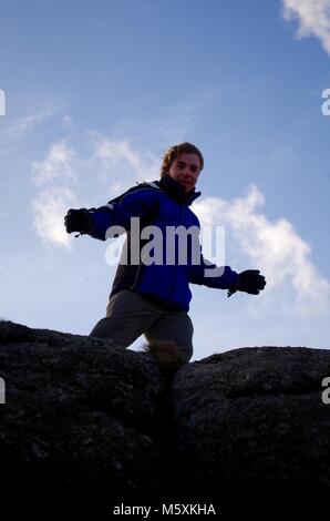 Junge männliche Hill Walker ontop der Granit Tor, von Haytor an einem windigen Wintertag. Nationalpark Dartmoor, Devon, Großbritannien. Stockfoto