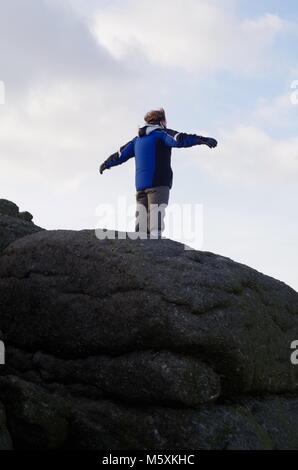 Junge männliche Hill Walker ontop der Granit Tor, von Haytor an einem windigen Wintertag. Nationalpark Dartmoor, Devon, Großbritannien. Stockfoto