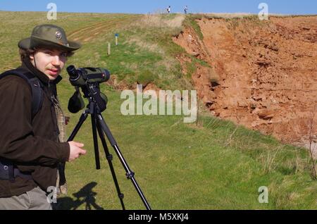 Junge schöne Vogelbeobachter mit Leica Spotting Teleskop. Auf dem South West Coast Path bei Budleigh Salterton, East Devon, Großbritannien. Jurassic Coast. Stockfoto