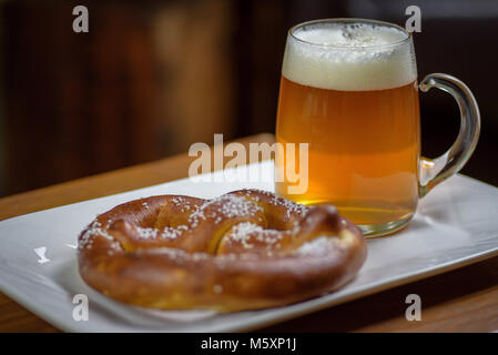 Makro Nahaufnahme von einem großen Glas Krug Bier und eine warme weiche Brezel auf einer Platte Stockfoto