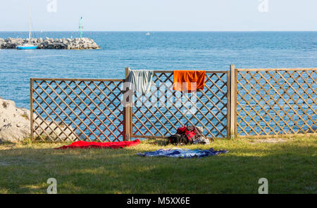Hölzerne Balustrade am Meer, mit Kleidung und einen Rucksack, ein paar Schuhe und ein Paar Badetücher auf dem Gras lehnte Stockfoto