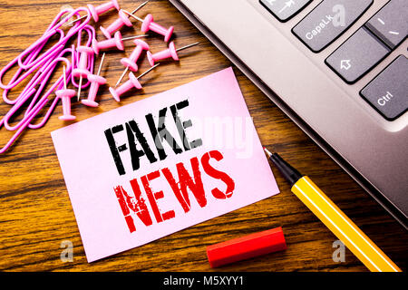Handschriftlichen Text, gefälschte Nachrichten. Business Konzept für Hoax Journalismus auf rosa Zettel Papier auf Holz- Hintergrund neben Tastatur geschrieben. Mit Stockfoto