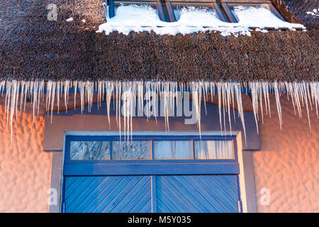 Gefährliche Eiszapfen an einem Strohhalm Zuckerrohr Dach. Das Konzept der Winter Wetter Stockfoto