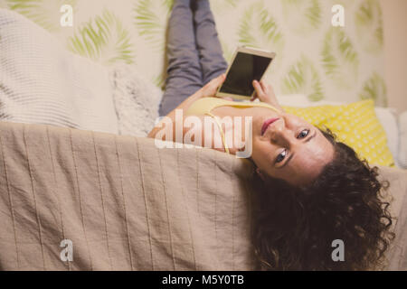 Schöne lockige liegende Frau auf dem Sofa und einem Tablet Stockfoto