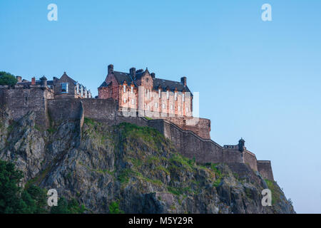 Steile Klippen mit Wänden und dem Krankenhaus Gebäude des Edinburgh Castle aus dem Norden unter einem blauen Himmel gesehen während des Sonnenuntergangs. Stockfoto