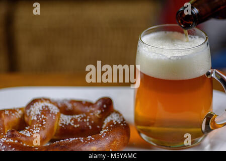 Bier zapfen in ein großes Glas mug auf Platte mit warmen weichen Brezel Vorspeise Stockfoto