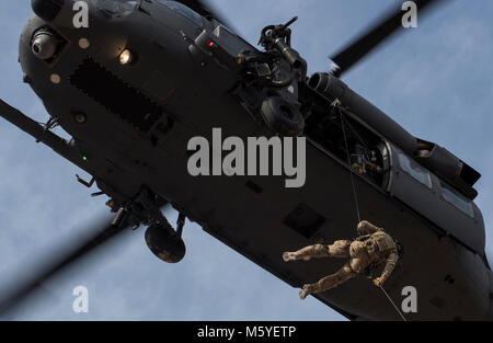 Eine pararescueman stößt aus HH-60G Pave Hawk Hubschrauber, die 66Th Rescue Squadron zugewiesen, während der Ausbildung auf der Nellis Air Force Base, Nevada, Feb 22, 2018. Die Pave Hawk ist ein mittlerer Hubschrauber mit Doppelrotor von Air Combat Command, Pacific Air Forces, Bildung und Ausbildung, der US-Luftstreitkräfte in Europa, Air National Guard und der Air Force Reserve Command betrieben. (U.S. Air Force Foto von älteren Flieger Kevin Tanenbaum) Stockfoto