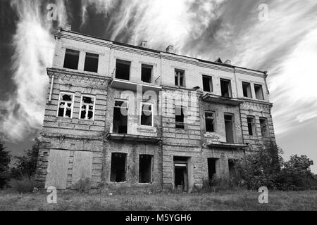 Alten, verlassenen Haus außen gegen die drastischen Schwarzweiß bewölkter Himmel ruiniert Stockfoto