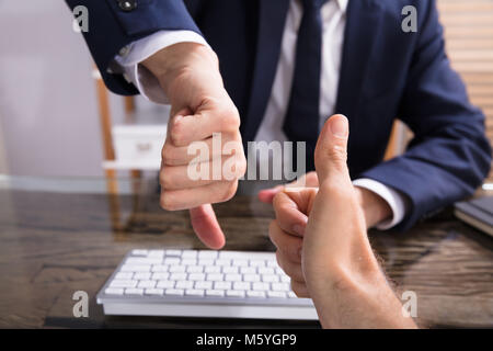 In der Nähe von zwei Geschäftsleute zeigen und Daumen hoch, Daumen runter Anmelden Büro Stockfoto