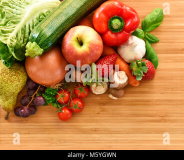 Gemüse und Obst Zusammensetzung oder Anordnung auf einem Bambus Schneidebrett. Frische Produkte, rote Paprika, Apfel, Möhren, Zwiebeln, Knoblauch, Erdbeere Stockfoto