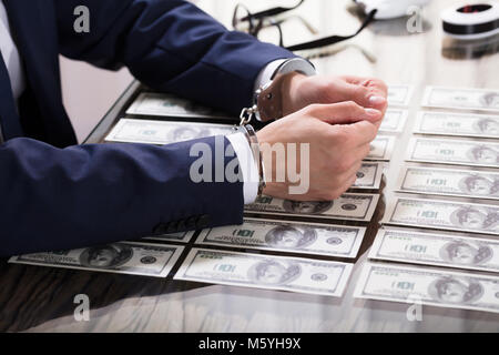 Unternehmer in Handschellen für Bestechung mit amerikanischen Banknoten auf dem Schreibtisch verhaftet Stockfoto