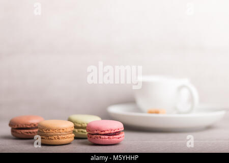 Verschiedene geschmackvolle Makronen mit einer Tasse Kaffee auf einem grauen Hintergrund Stockfoto