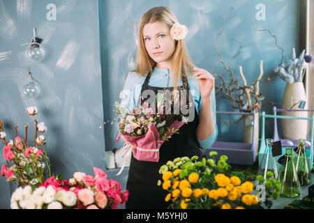 Junge Frau, die unter den verschiedenen Blumen und Holding Zusammensetzung Stockfoto