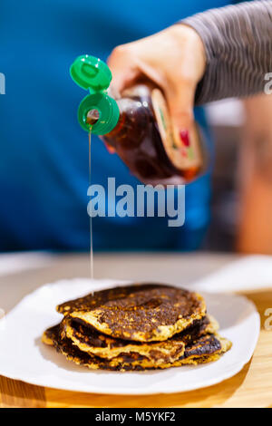 7/8 Schuß von Person gießen Ahornsirup auf Stapel Pfannkuchen Stockfoto