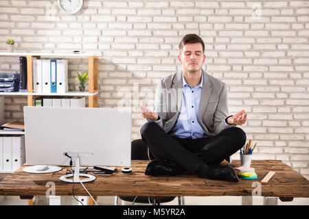 Junge Unternehmer sitzen auf hölzernen Schreibtisch Meditieren im Büro Stockfoto