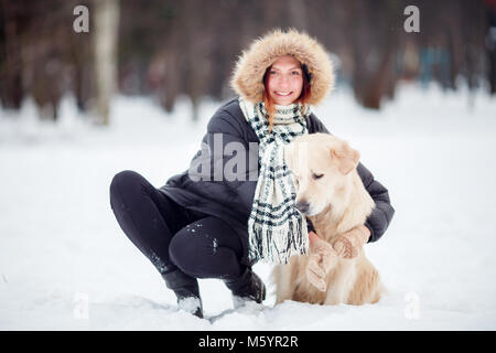 Bild von Mädchen in schwarzen Jacke hocken neben Hund im Winter Stockfoto