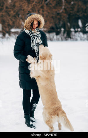 Bild der Frau in den schwarzen Jacke mit Retriever auf Spaziergang im Winter Park Stockfoto