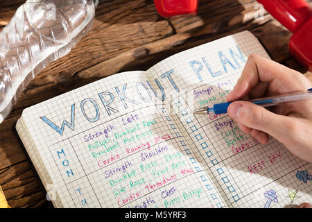 Erhöhten Blick auf eine Person, die Kenntnis von Workout Plan auf dem Notebook mit Trainingsgeräten Stockfoto