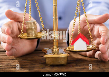 Nahaufnahme von einer Person die Hand zum Schutz des Rechts Skala mit gestapelten Münzen und Haus Modell Stockfoto