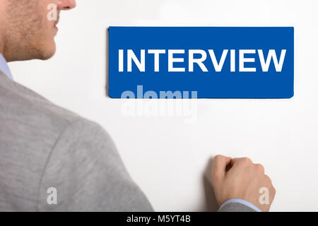 Nahaufnahme eines Junge Unternehmer klopfen weiße Tür mit Interview Typenschild Stockfoto