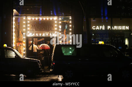 Ein Spaziergänger schützt sich vor dem Regen unter ihrem Regenschirm, der an einem Taxistand und einem Café in Belfast im Stadtzentrum vorbeigeht Stockfoto