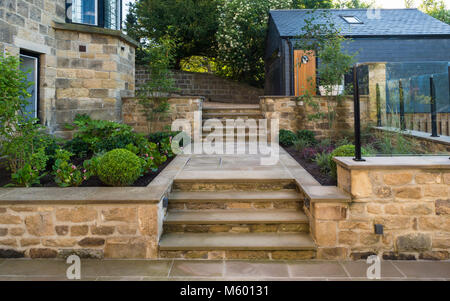 Kleine Ecke des schönen, gepflegten, privaten Garten mit zeitgenössischem Design, gepflasterter Weg & Schritte, Sträucher und Pflanzen - Yorkshire, England, UK. Stockfoto