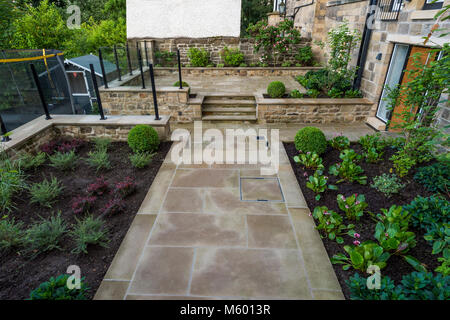 Kleine Ecke des schönen, gepflegten, privaten Garten mit zeitgenössischem Design, gepflasterter Weg & Schritte, Sträucher und Pflanzen - Yorkshire, England, UK. Stockfoto