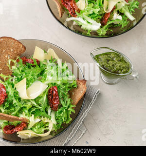 Salat mit frisee Eisbergsalat, sonnengetrocknete Tomaten, Käse, Brot, Chips und Pesto Dressing, Quadrat Zusammensetzung Stockfoto