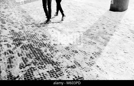 Beine von zwei Menschen zu Fuß die schneebedeckte Bürgersteig in motion blurin Schwarz und Weiß Stockfoto