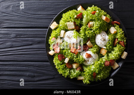 Gourmet Salat Lyonnaise mit Salat, knusprigem Speck, Croutons und pochierte Eier close-up auf einem Teller auf den Tisch. Horizontal oben Ansicht von oben Stockfoto