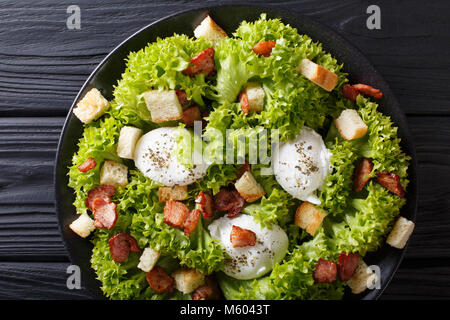 Organische französischen Lyonnaise Salat mit Salat, Speck, Croutons und pochierte Eier close-up auf einem Teller auf den Tisch. horizontal oben Ansicht von oben Stockfoto